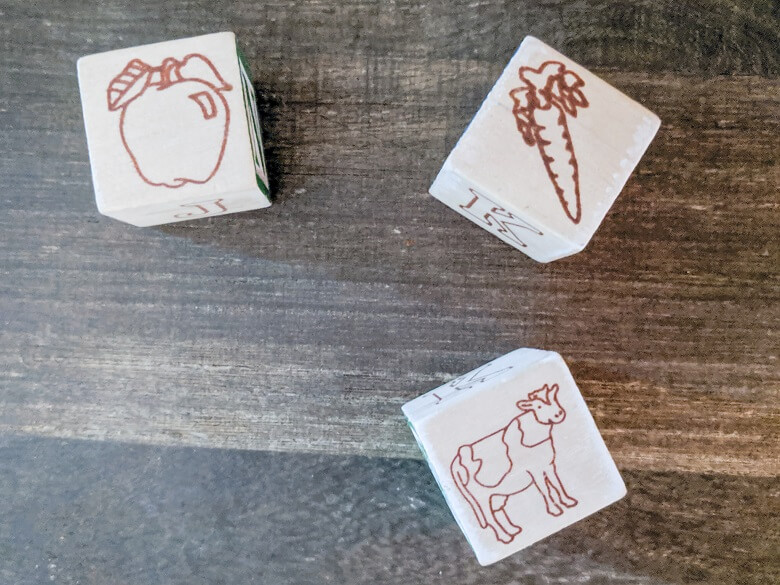 Three wooden toy blocks with shapes of an apple, carrot and cow.