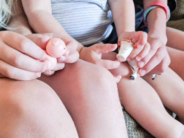 A close up of three children's knees while they sit on a couch and hold farm animal toys in their laps.