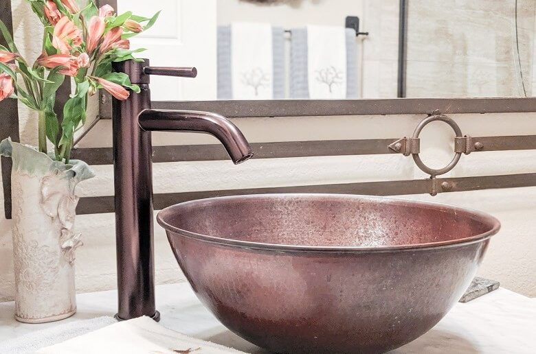 A copper sink in a bathroom with flowers next to it.