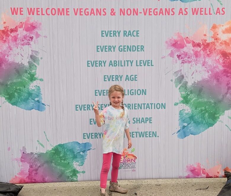 Young girl standing in front of a sign for Vegan Sunday festival