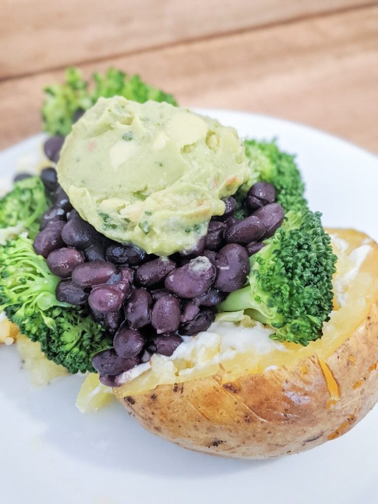 a vegan baked potato dinner consisting of a baked potato, vegan butter and sour cream, broccoli, black beans and guacamole