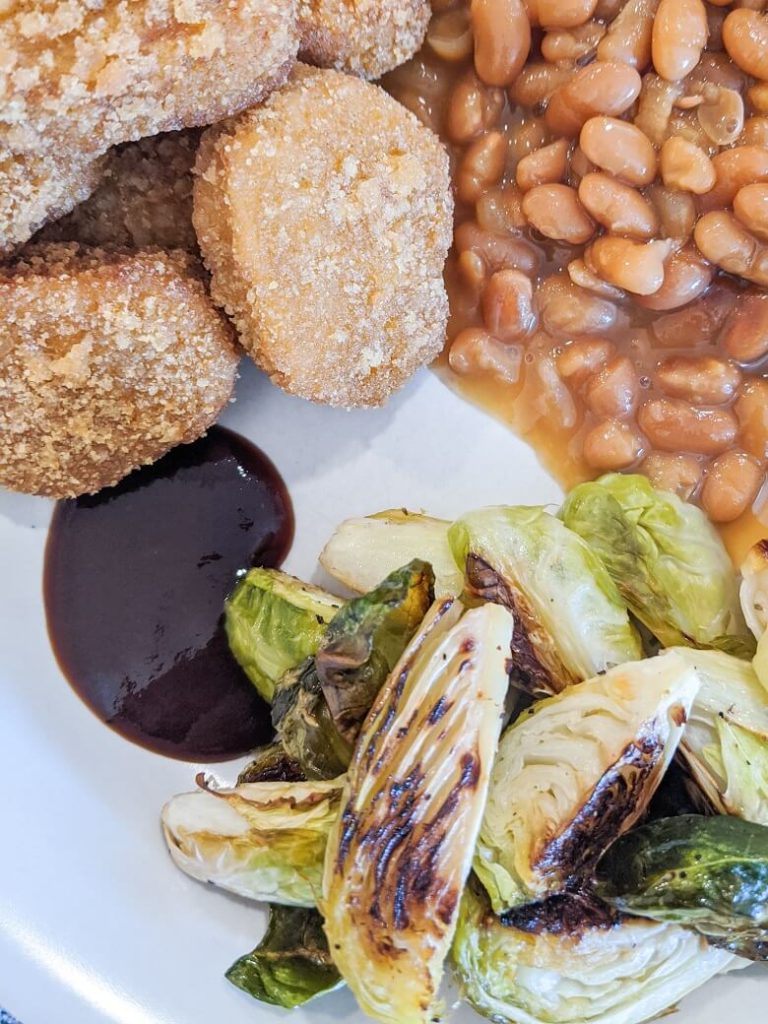 a vegan family dinner consisting of chik'n nuggets, baked beans, Brussels sprouts and barbecue sauce