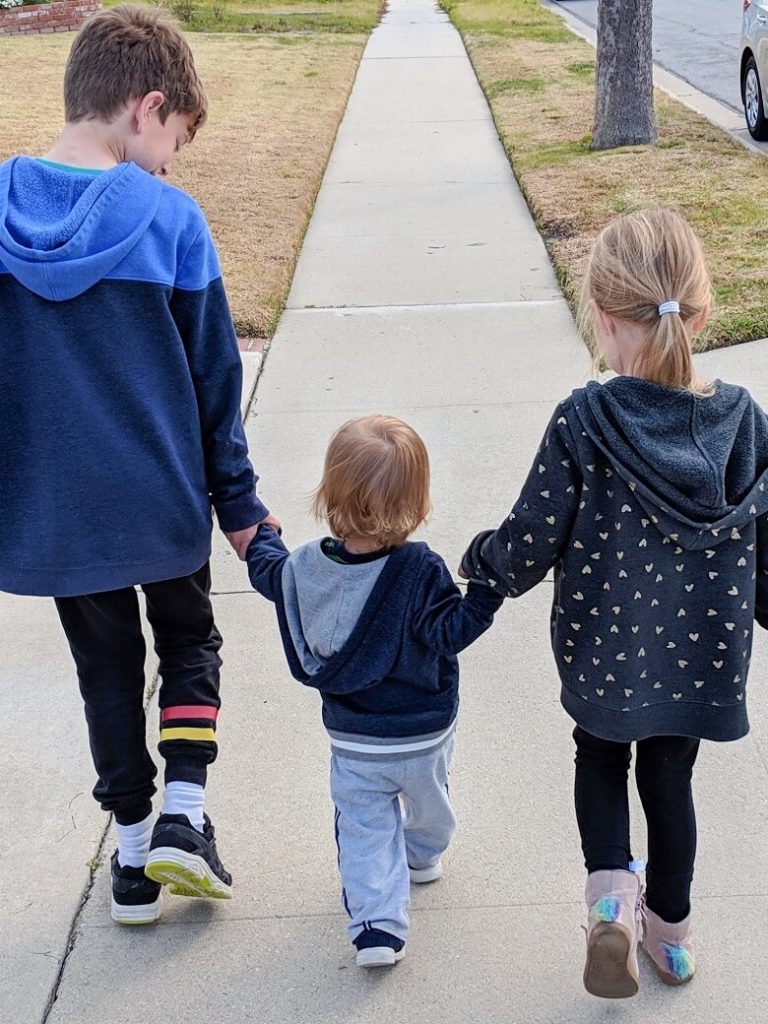 Three children of different ages holding hands as they walk mindfully on a sidewalk enjoying a mindful moment