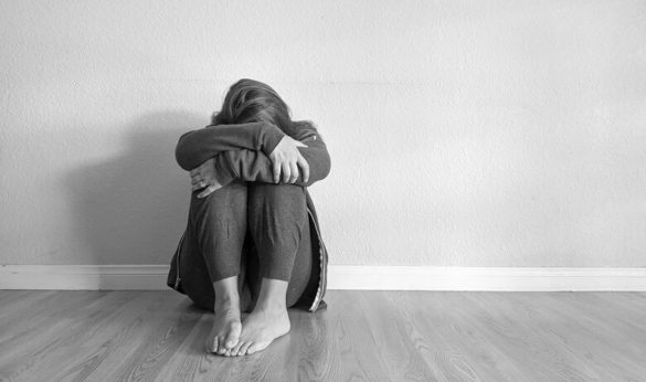 A woman struggling with anxiety sitting on the floor with her arms wrapped around her knees and her head down