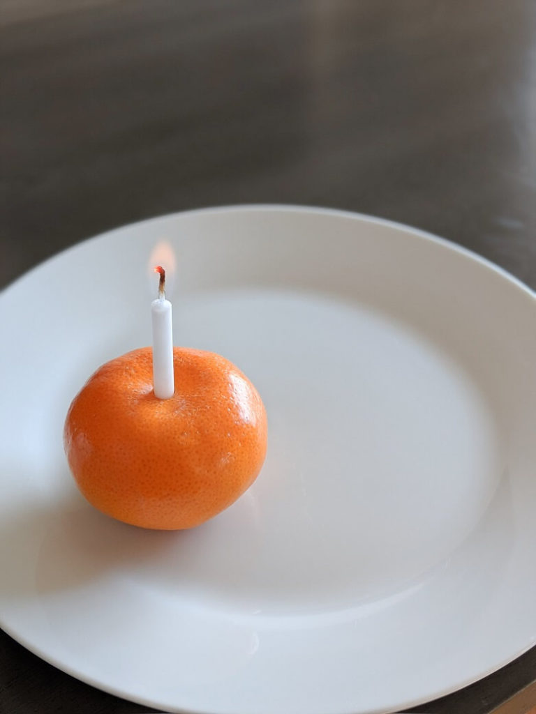 A picture of an orange on a plate with a lit candle in the center of it.