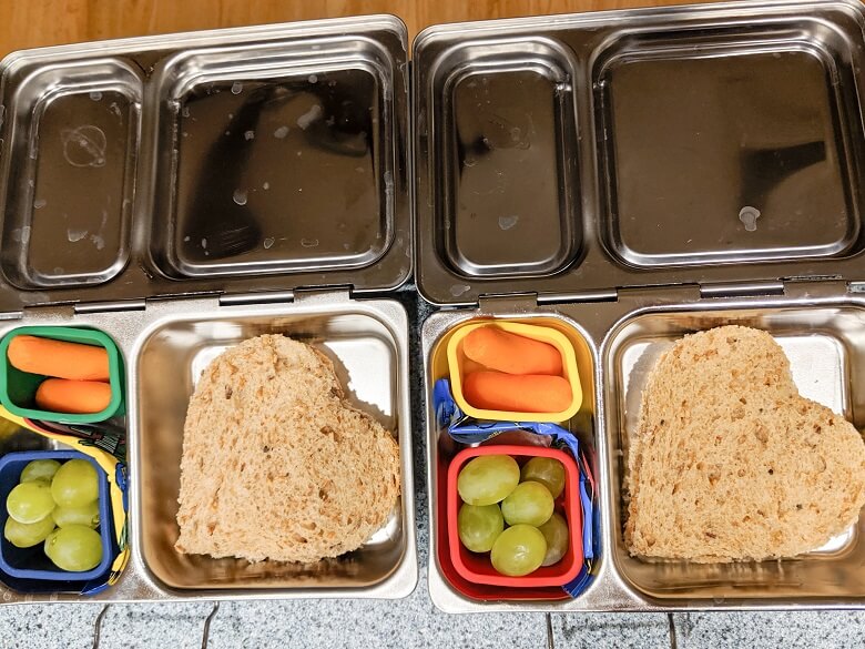 Vegan lunches for kids of nut butter and jam sandwiches cut like hearts, carrot sticks, grapes and fruit wrap