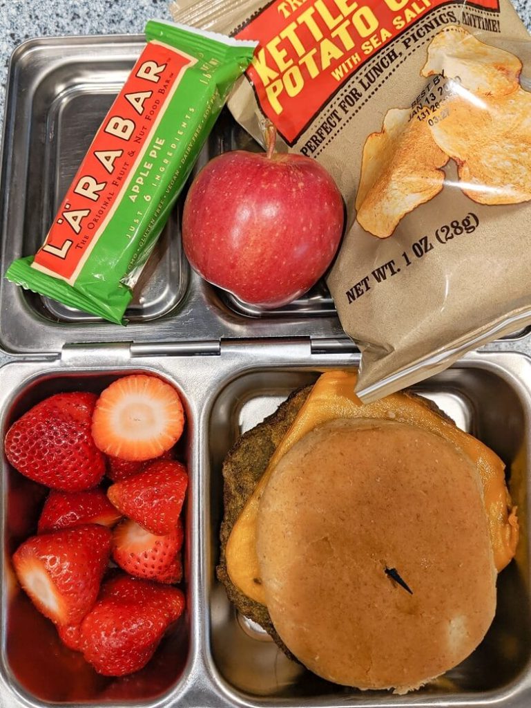 Quick vegan lunch for school of strawberries, veggie burger, Larabar, apple and potato chips