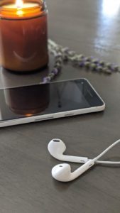 Headphones, a phone, lavender and a candle burning to show listening to music to reduce anxiety