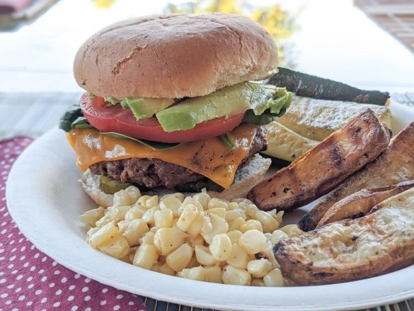 Beyond burger with toppings alongside vegan BBQ sides of corn, potato wedges and zucchini