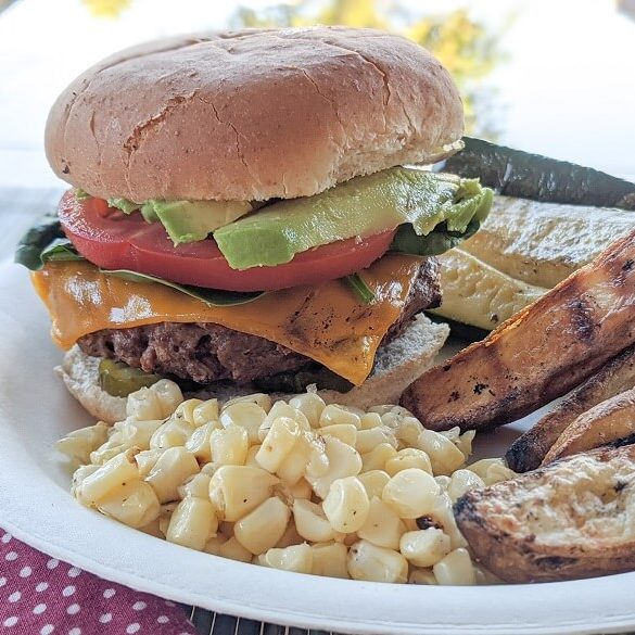 Beyond burger with toppings alongside vegan BBQ sides of corn, potato wedges and zucchini