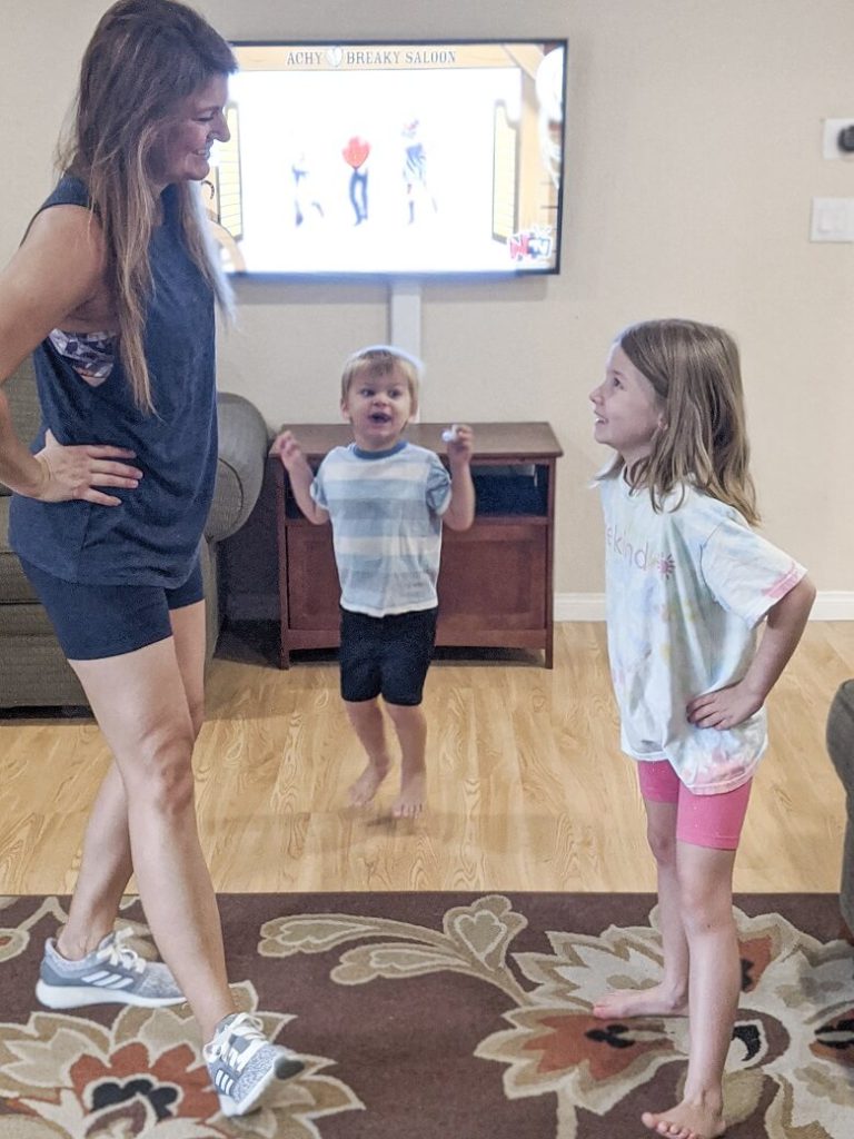 Mom working out at home with her kids by dancing with her young daughter and toddler son
