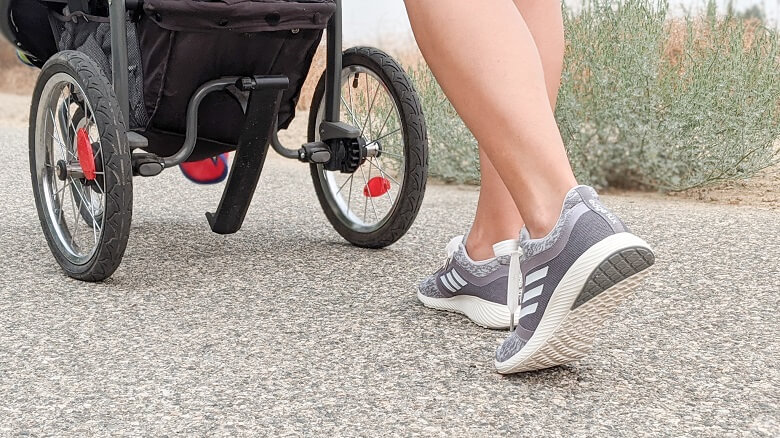 A woman's shoes walking on a path as she pushes a stroller to show options for working out at home with kids.