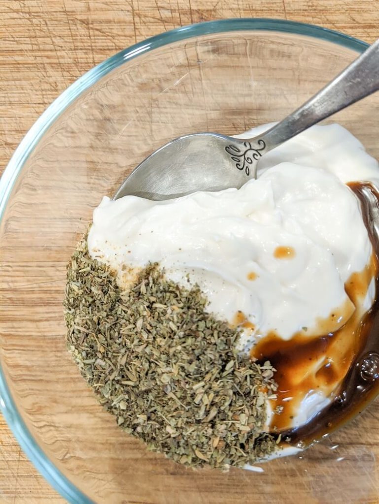 A bowl with the ingredients for a vegan artichoke dipping sauce which include vegan mayonnaise and Worcestershire sauce, Italian seasonings and garlic powder.