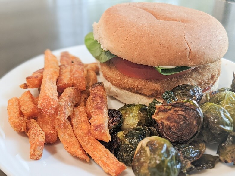 A vegan family meal consisting of a chickless sandwich and sweet potato fries and Brussel sprouts