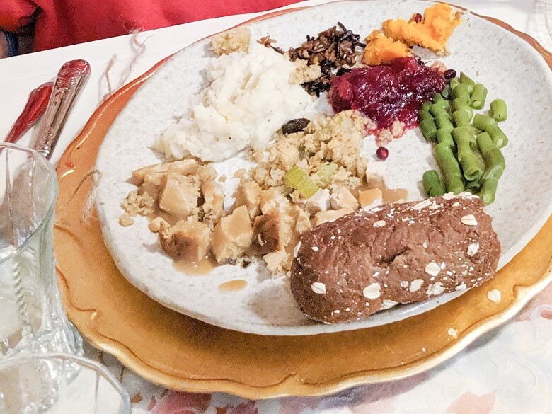 A kid's plate at a vegan Thanksgiving filled with mashed potatoes, green beans, cranberries, yams, wild rice, stuffing, vegan roast, and a roll