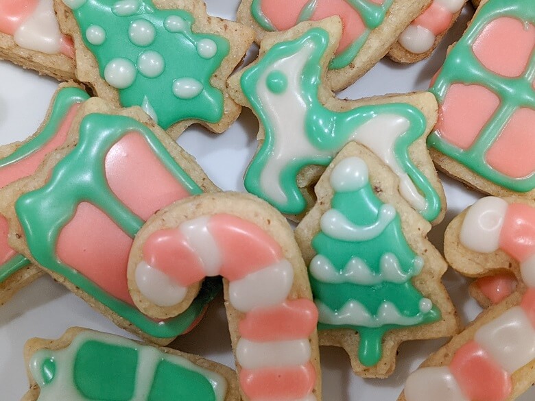 Christmas cookies with vegan icing decorations, some cut outs include a Christmas tree, candy cane, reindeer and a present.