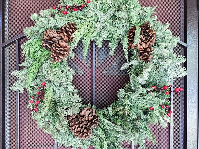 A wreath with real leaves and pinecones hanging on a front door
