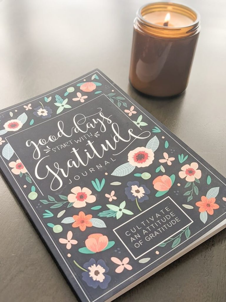 A gratitude journal on a table with a candle burning in the background.