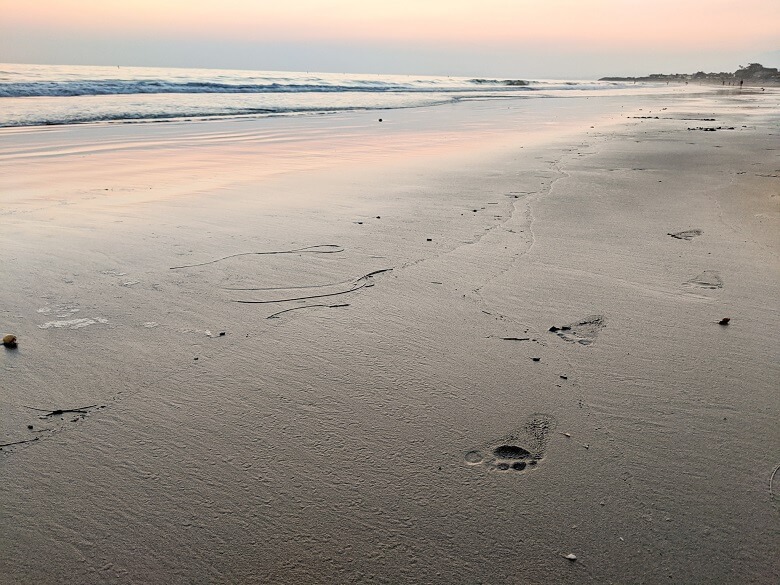 A beach with calm waters at sunset with footprints in the sand to show how to find peace with a mindful walk.