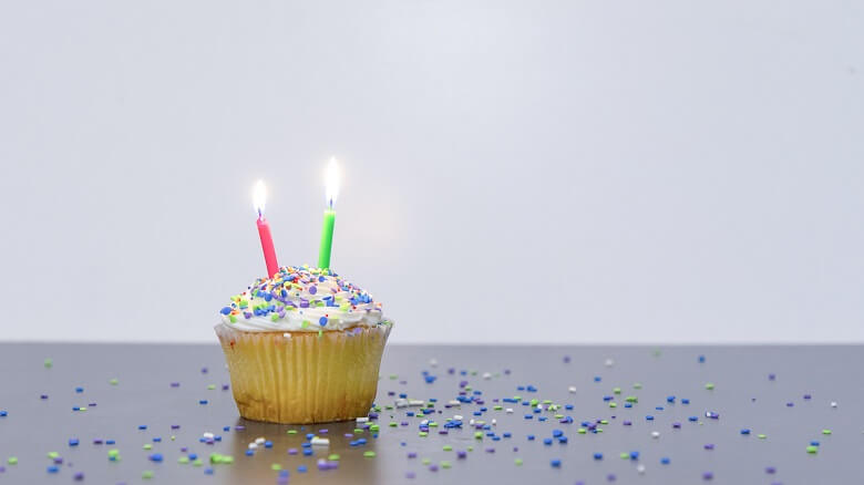 A cupcake with two lit candles to represent our second veganniversary (2 years of being vegan) and lots of sprinkles on the table around the cupcake.