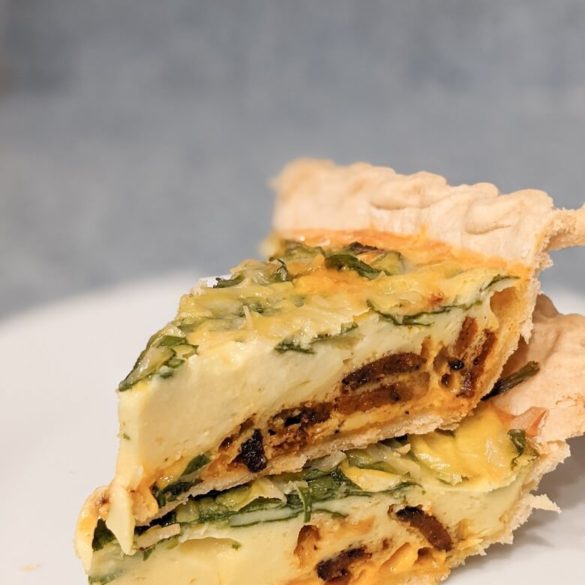 Two slices of vegan quiche stacked on top of each other. The inside of the quiche shows spinach, melted vegan cheeses, vegan bacon, and cooked JUST Egg.
