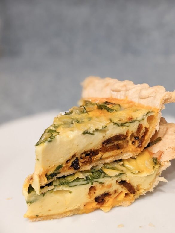 Two slices of vegan quiche stacked on top of each other. The inside of the quiche shows spinach, melted vegan cheeses, vegan bacon, and cooked JUST Egg.