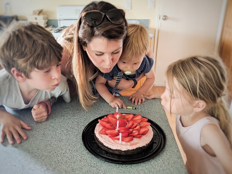 A SAHM with her three kids blowing out candles on a birthday cake.