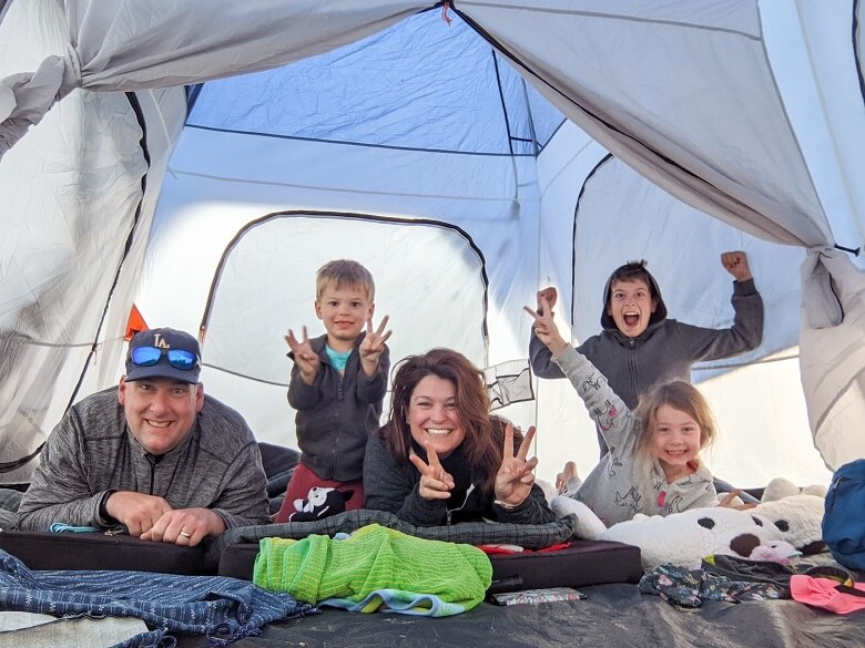 A vegan family of five camping in a tent, smiling a the camera