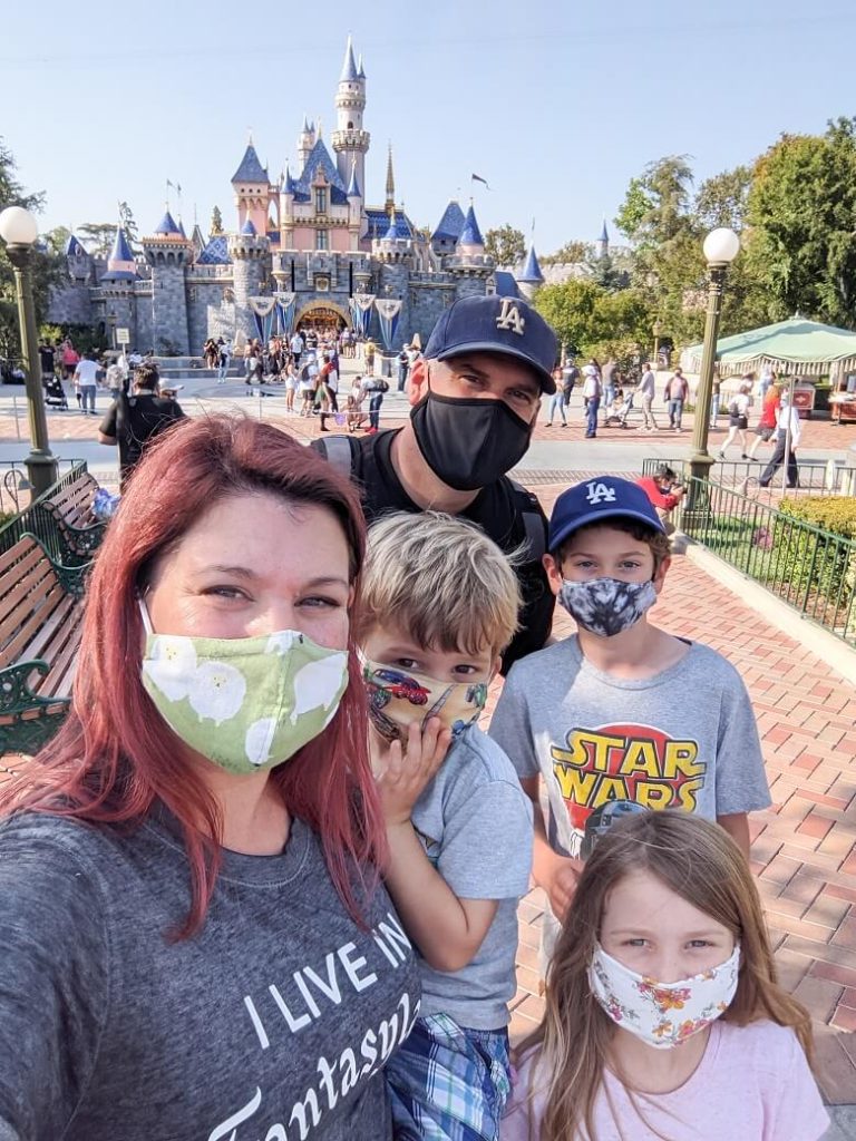 A family with a woman and man and three young kids wearing masks with Disneyland castle in the background.
