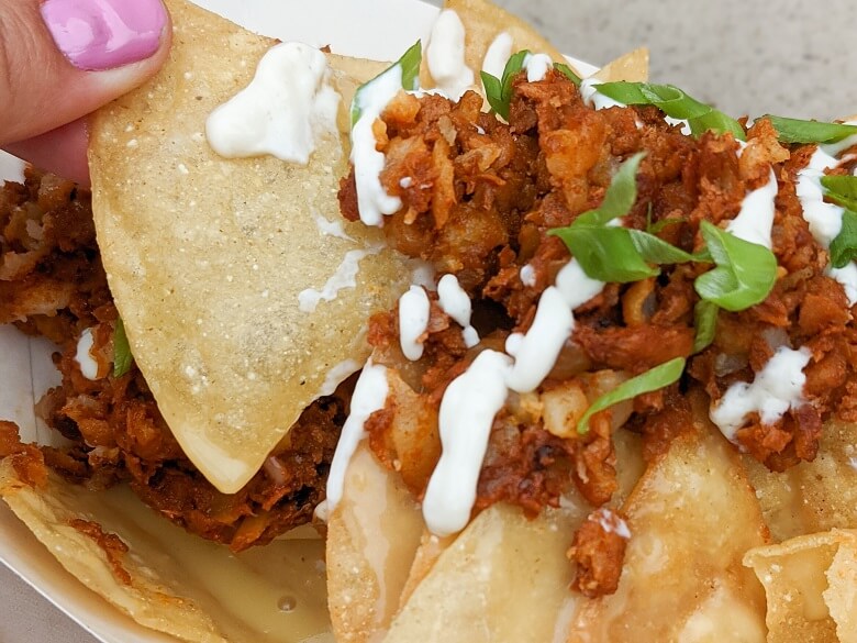 A woman's finger pulling a chip away from vegan nachos topped with soy chorizo and diary free crema.