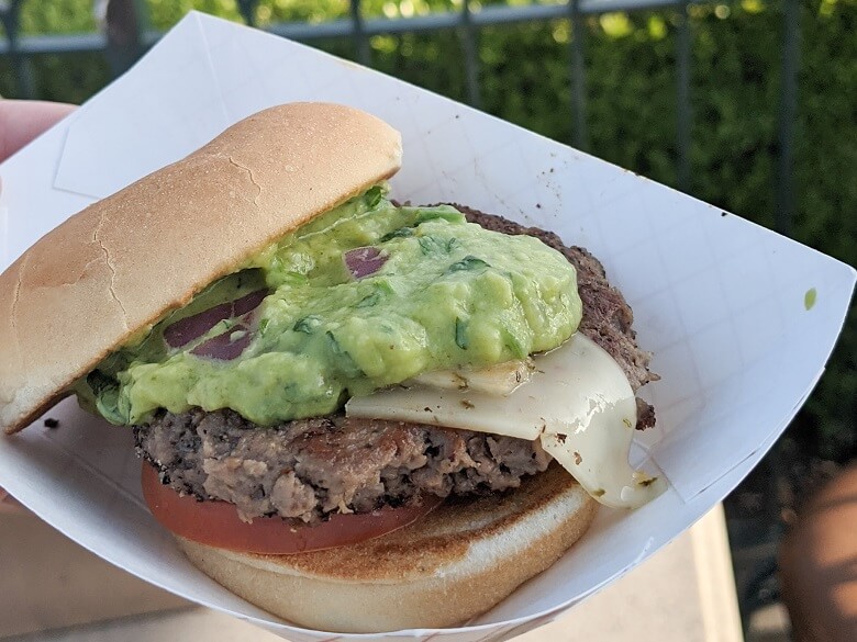 A small vegan burger with pepper jack cheese and a dollop of guacamole and a tomato between a toasted bun. Served on a paper plate in Disney California Adventure.