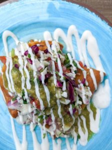 Two vegan potato tacos topped with a cabbage slaw and dairy-free crema on a plate.