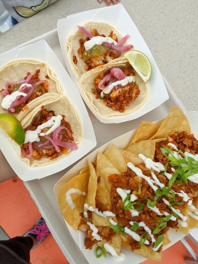 Vegan food at Disney California Adventure from Hollywood Lounge Studio Catering Truck that includes the Plant-Based Backlot Nachos which are chips covered in soy chorizo and dairy-free crema with some green onions and Potato and Soy Chorizo Tacos which are two street tacos with a lime wedge on the side.