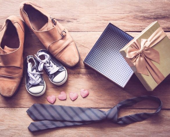 A pair of mens shoes next to a pair of child's shoes, alongside a tie, four small hearts and a gift box to show presents for dad