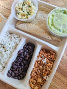 A vegan kids meal from Chipotle that includes a to-go box with two tortillas, corn salsa, guacamole, rice, beans and sofritas