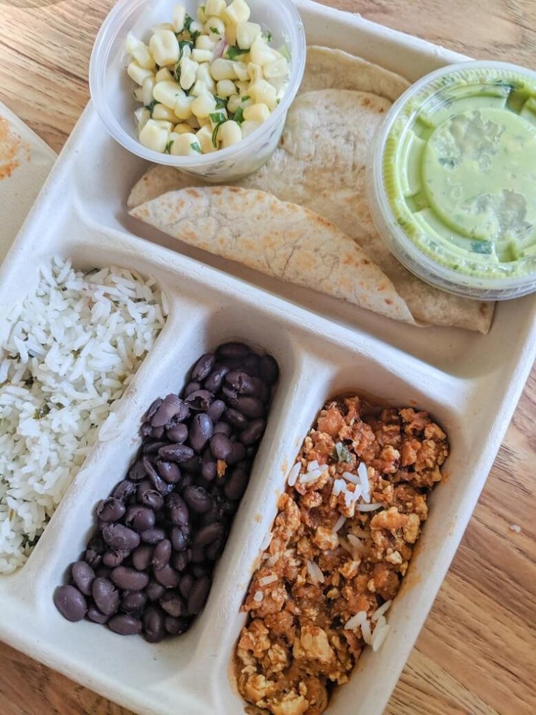 A vegan kids meal from Chipotle that includes a to-go box with two tortillas, corn salsa, guacamole, rice, beans and sofritas