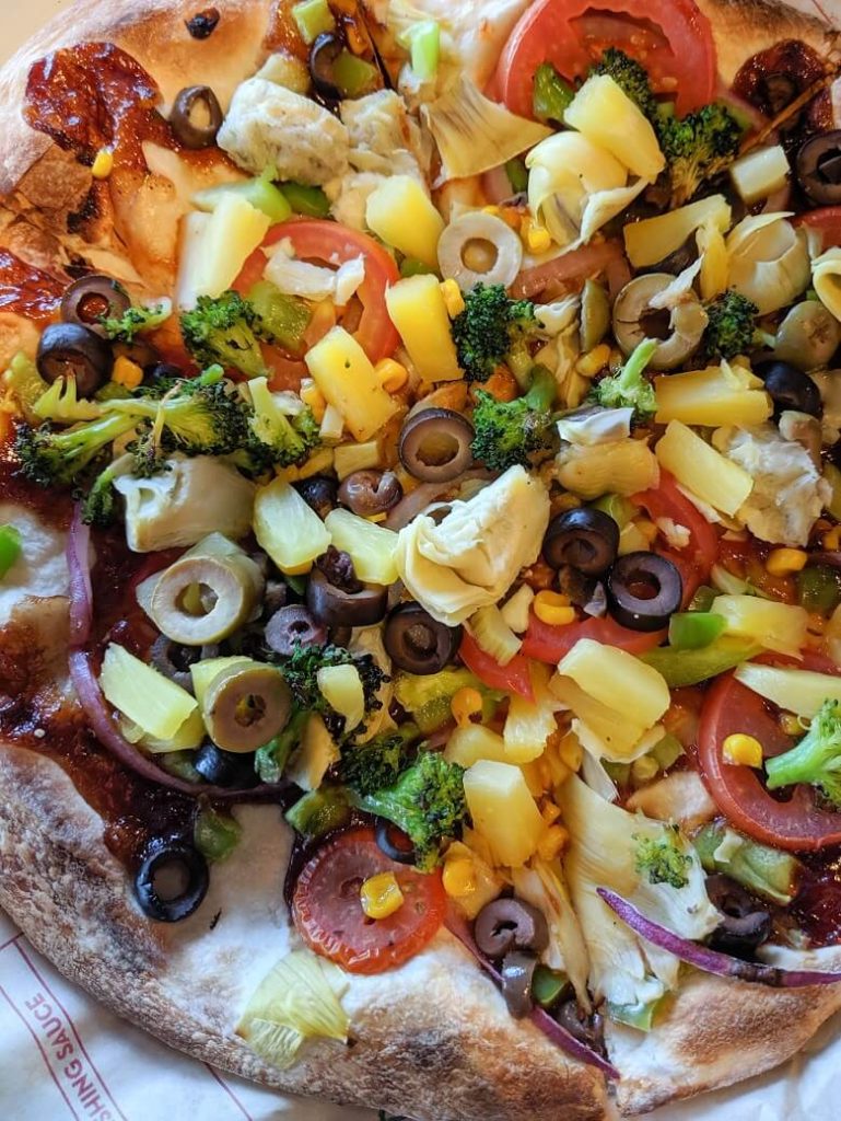 Vegan pizza from MOD Pizza with no cheese and olives, pineapples, artichoke hearts, tomatoes, broccoli, onions, corn, and garlic