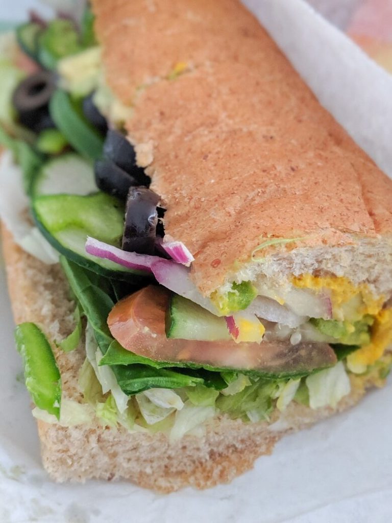 Vegan sub sandwich from Subway with olives, onions, mustard, cucumbers, tomatoes, lettuce, peppers and avocado