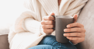 A woman's hands holding a mug while resting on a couch