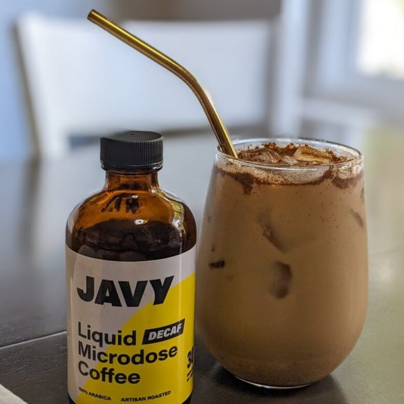 A bottle of Javy Coffee concentrate next to an iced brown sugar oat milk latte in a clear glass with a copper straw.