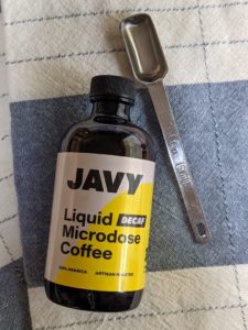 A bottle of decaf Javy Coffee liquid microdose coffee on a dish towel next to a teaspoon.