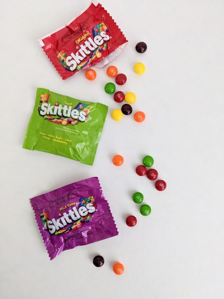 Three bags of Skittles with one of them open and several candies spread out.