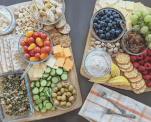 Two wooden cutting boards on a table. One has vegan dip, jam, almonds, pears, crackers, raspberries, blueberries, grapes and vegan cheese. The other one has tabouli, Persian cucumbers, green olives, vegan cheeses, lavash, grape tomatoes, crackers, marinated artichoke hearts, hummus and cashews.