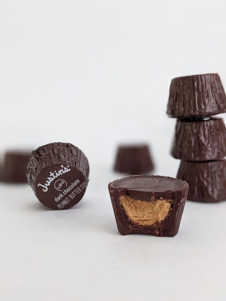 Several wrapped mini Justin's Dark Chocolate Peanut Butter Cups. One is open with a bite out of it. The others are wrapped.