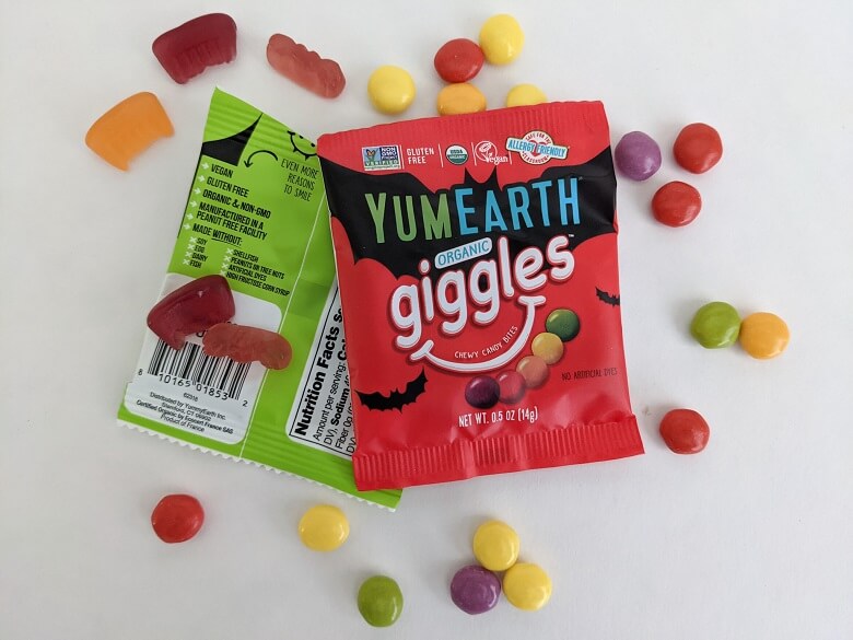 A bag of YumEarth Giggles and Fruit Snacks with several open and spread out around the bags.