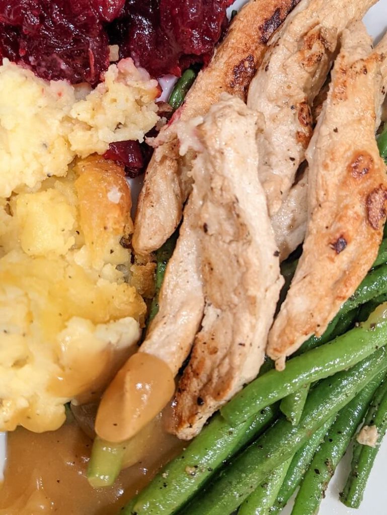A plate of mashed potatoes, cranberries, green beans and vegan turkey strips.