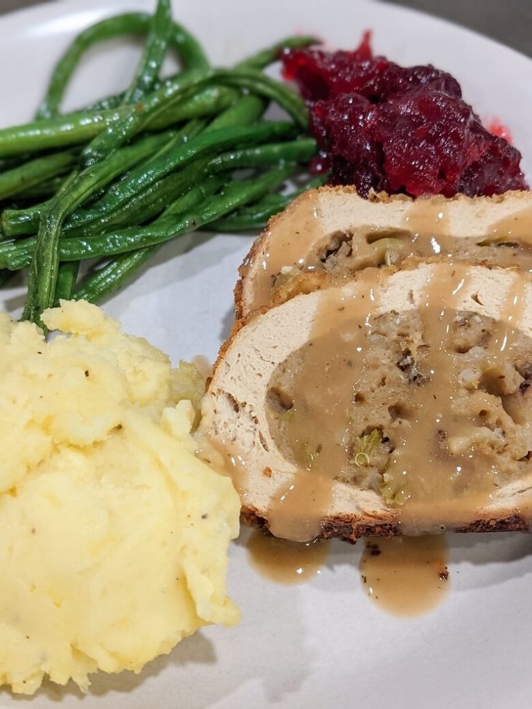 A Thanksgiving dinner with a sliced vegan roast, mashed potatoes, green beans, and cranberries.