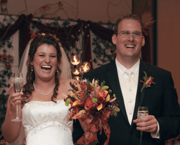 A happy bride and groom on their wedding day holding glasses of champagne, and laughing hysterically during a toast.