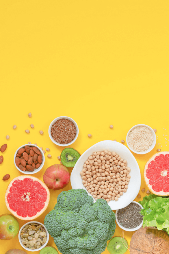 A yellow background with various fruits, vegetables, beans, seeds, and nuts sprinkled all over to show inspiration to eat more plants.