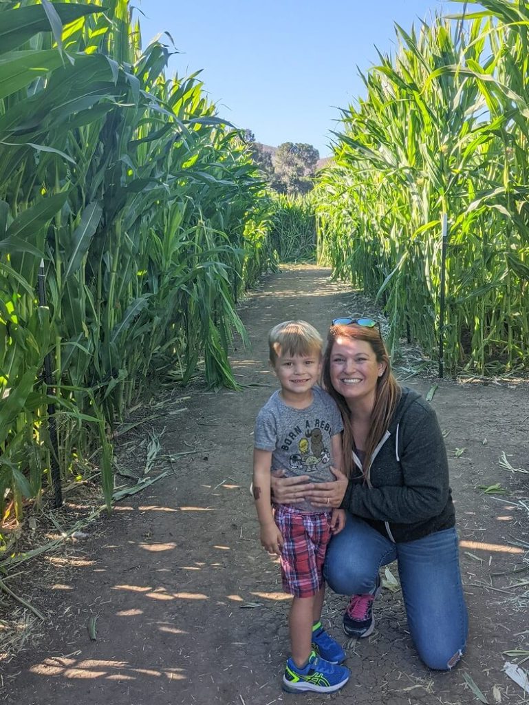 Mother kneeling next to her young son in a corn maze.